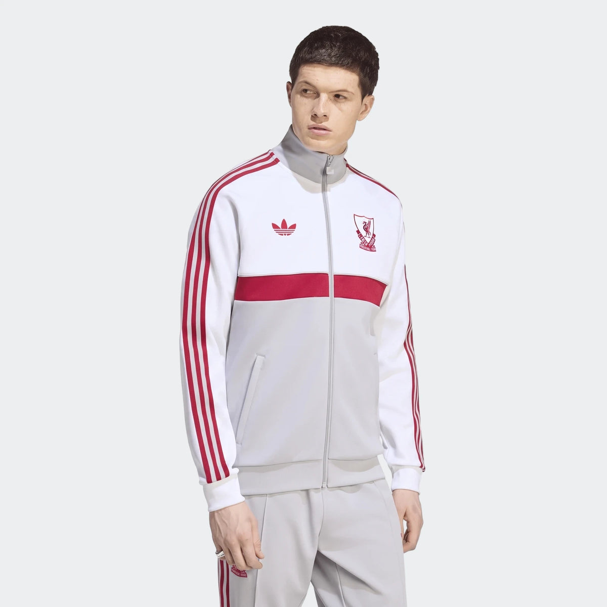 White, red, and grey Liverpool FC Originals track top on a male model, featuring Adidas stripes and the club crest.