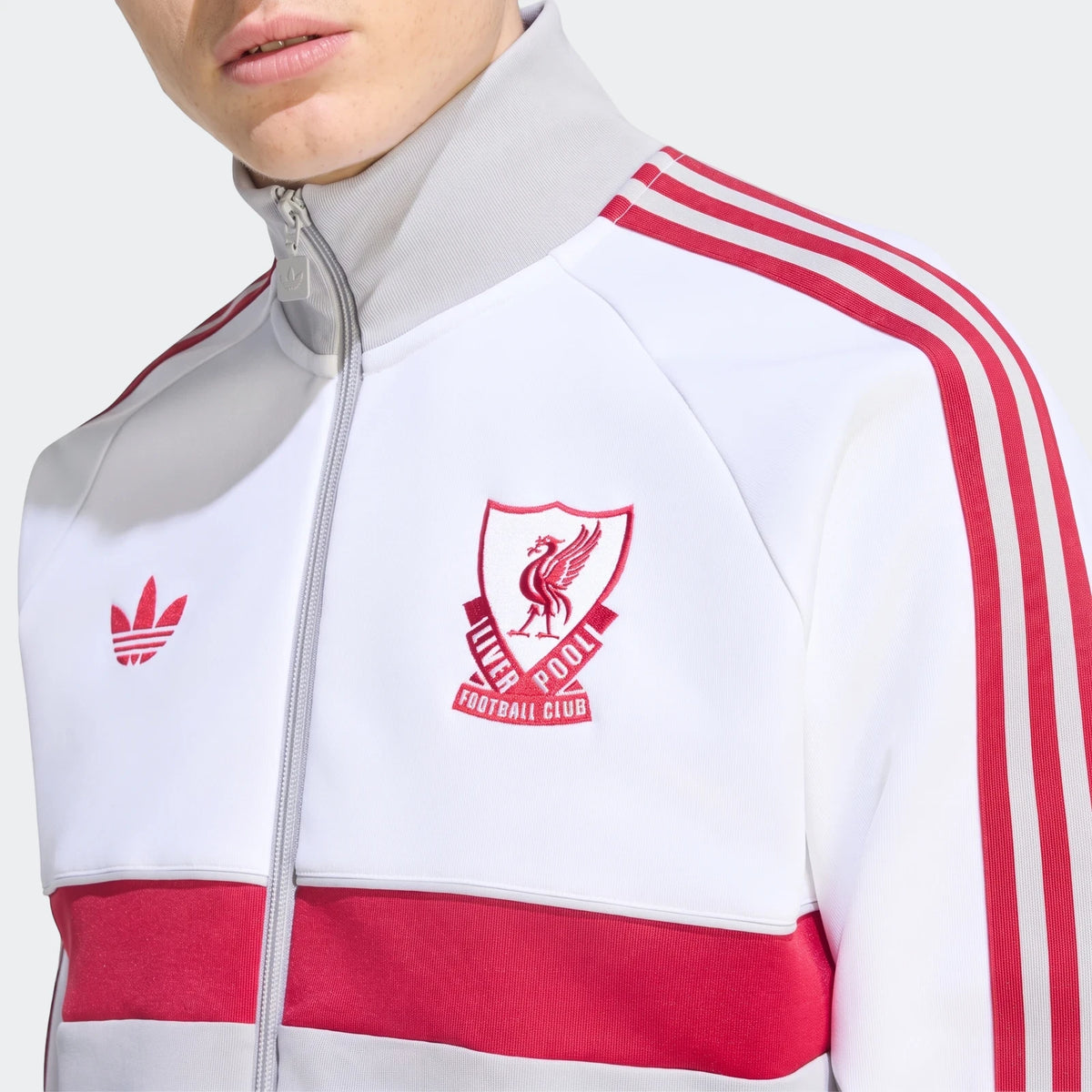 Close-up of a white Liverpool FC Originals track top with red stripes and crest, worn by a person.