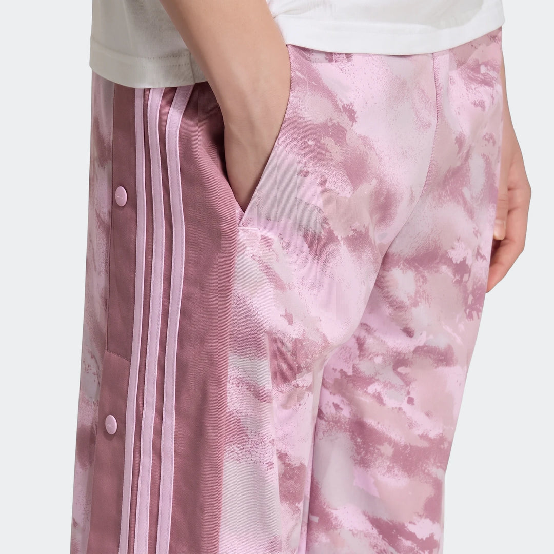 Close-up of a person wearing pink camouflage Loose Adibreak Camo Twill Trousers with light pink side stripes and snap