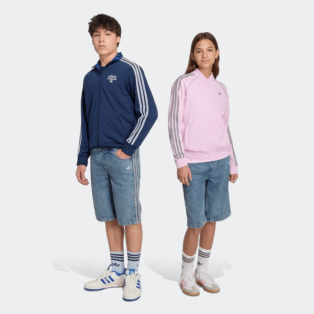 Two models wearing light wash loose denim jorts with side stripes, paired with Adidas track jackets and sneakers, full body
