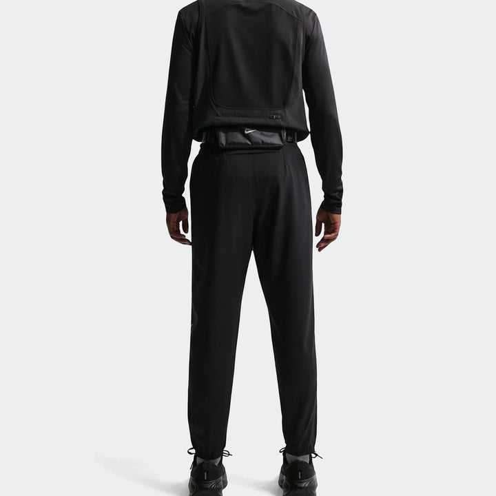 Men's Nike Dri-Fit Miler Woven Pants in black, shown from the back with a long-sleeved top, fanny pack, and athletic shoes.