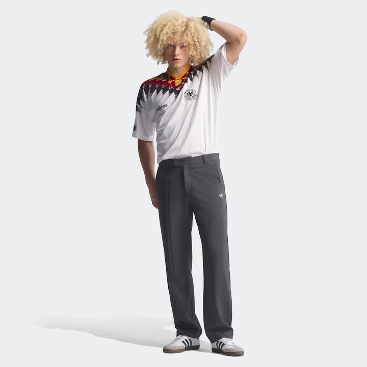 Male model wearing a white Adidas football jersey with black, red, and yellow accents and dark grey Adidas track pants.