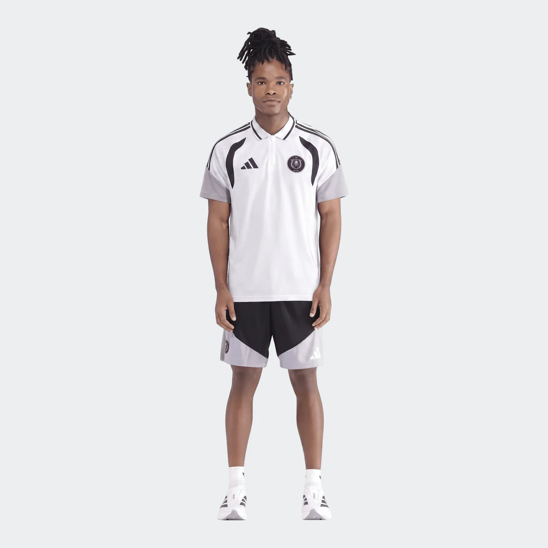 Male model wearing a white Adidas Op Tiro26C Polo shirt with black and grey accents and matching shorts, full body view.