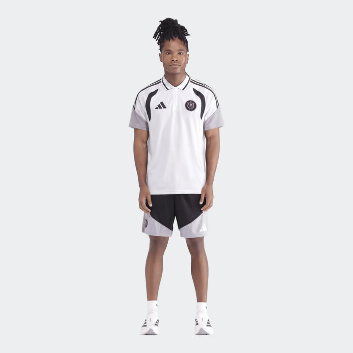 Male model wearing a white Adidas Op Tiro26C Polo shirt with black and grey accents and matching shorts, full body view.
