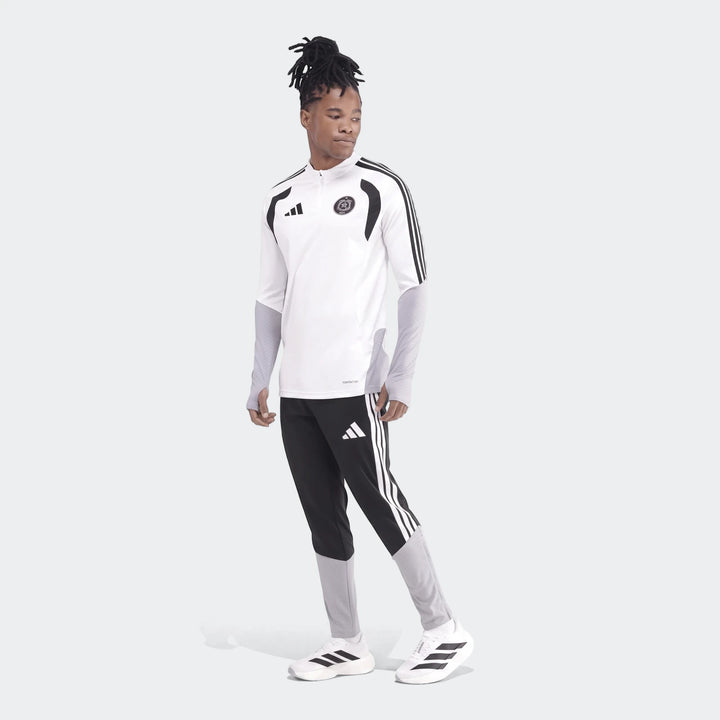 Male model wearing a white Adidas Op Tiro26C Top with black and grey track pants and white sneakers, side view.