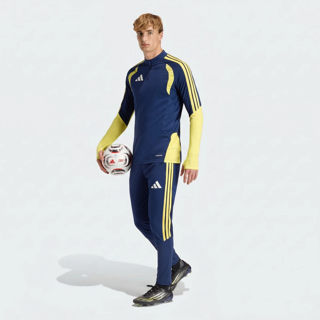 Male model wearing blue and yellow Adidas Tiro26 C Pant Blue Pants and matching tracksuit top, holding a soccer ball.