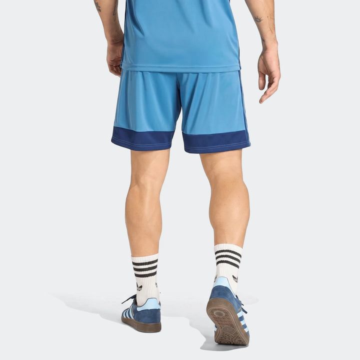 Male model from back wearing blue and dark blue Tiro Essentials Shorts with matching blue top, white striped socks, and blue