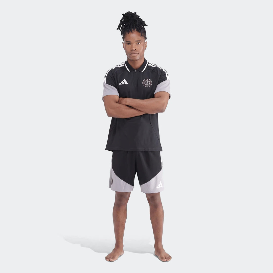 Male model wearing a black and grey Adidas Op Tiro26C Polo shirt and matching shorts, standing with arms crossed.