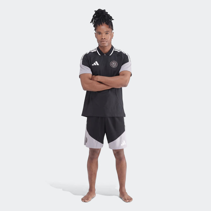 Male model wearing a black and grey Adidas Op Tiro26C Polo shirt and matching shorts, standing with arms crossed.