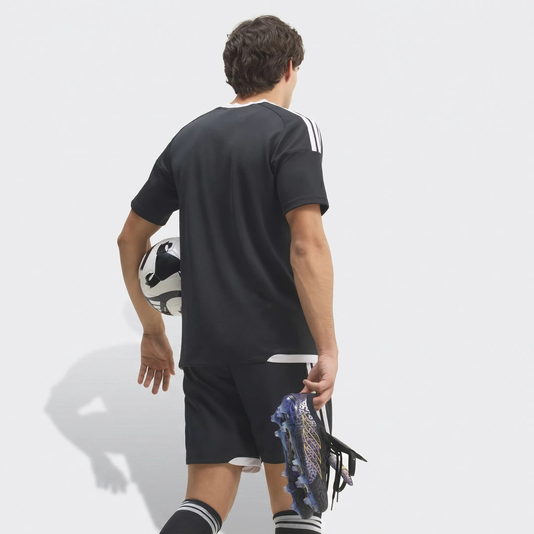 Rear view of a male model wearing a black football kit, holding Predator Elite Ft Fg Kaka Edition Football Boots and a