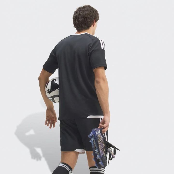Rear view of a male model wearing a black football kit, holding Predator Elite Ft Fg Kaka Edition Football Boots and a