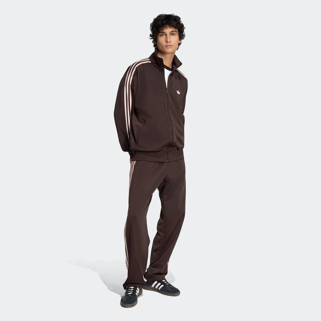 Male model wearing a full brown Adidas Firebird Track Top and matching track pants with three stripes, paired with black