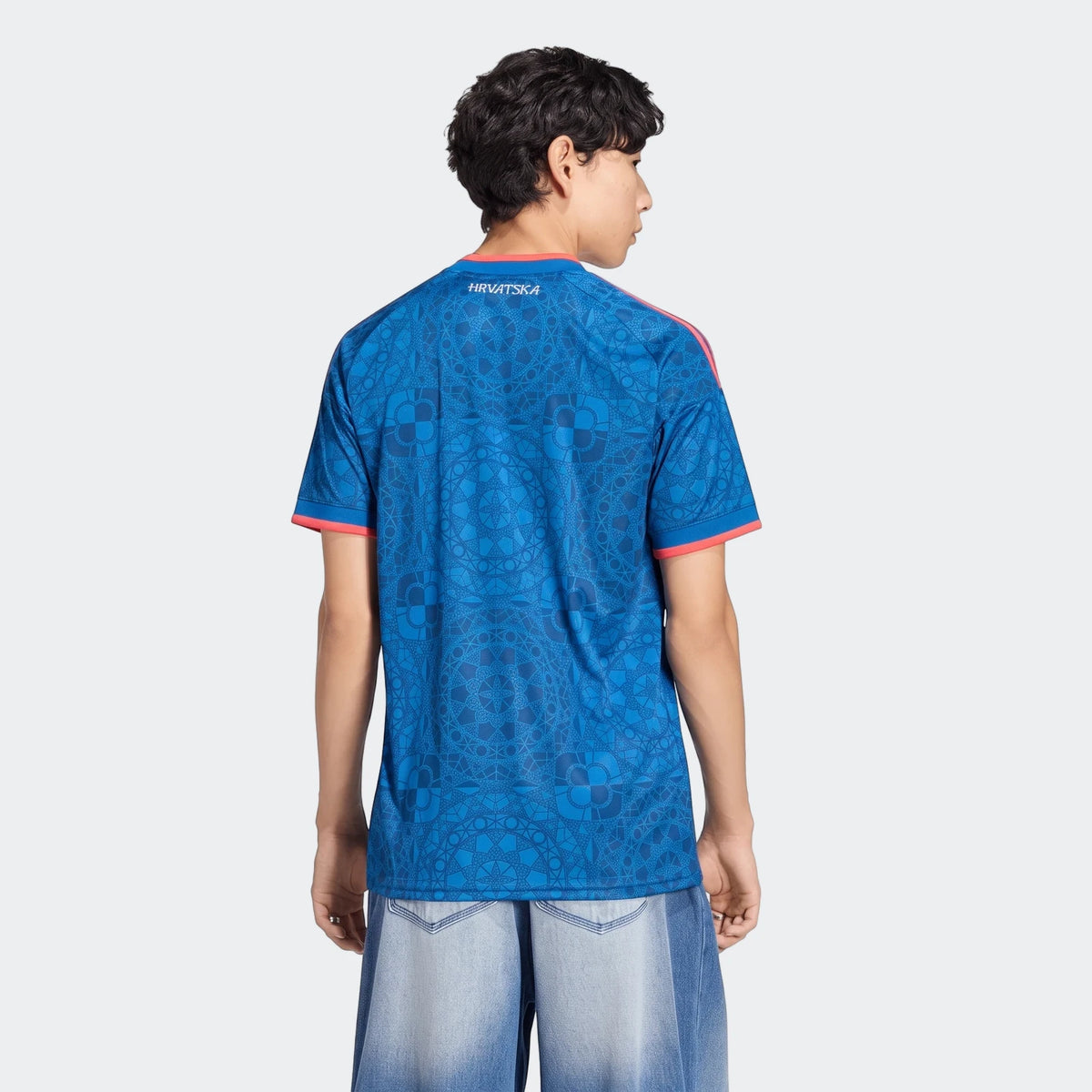 Male model wearing a blue patterned Croatia 26 Away Jersey, seen from the back, paired with light blue jeans.