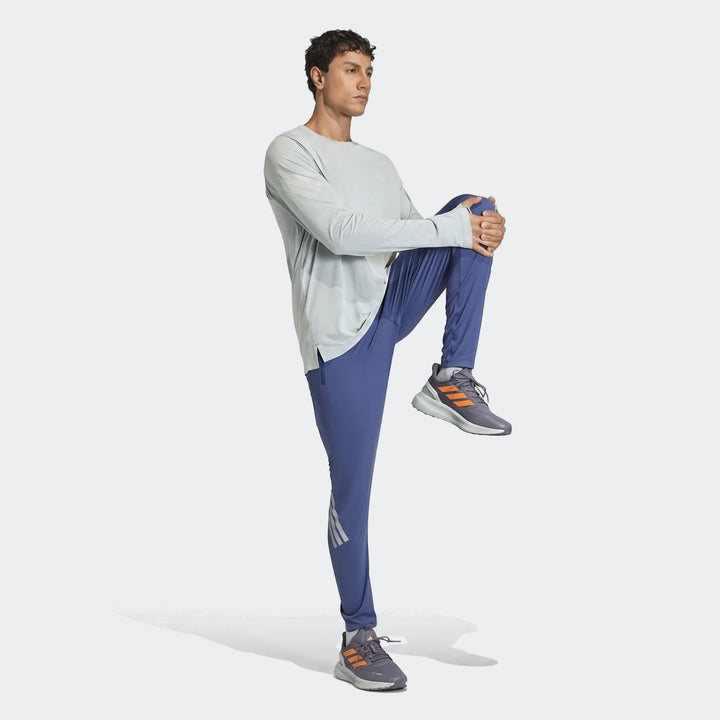 Male model wearing light grey long-sleeve top, blue Adi365 Track Pants, and grey-orange running shoes, posing with one knee