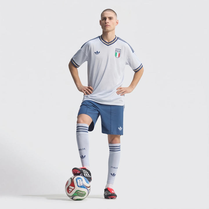 Male model wearing a white and blue Italia soccer jersey, blue shorts, and socks, standing with a soccer ball.