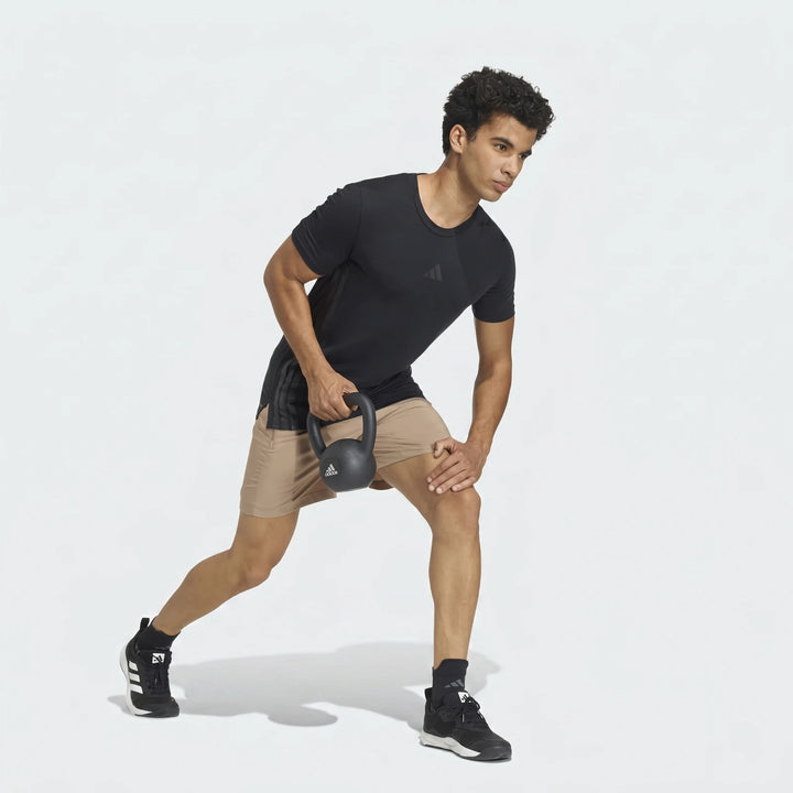 Male model in black t-shirt and khaki Adidas Workout Essentials Base Woven Shorts performing a lunge with a black kettlebell.