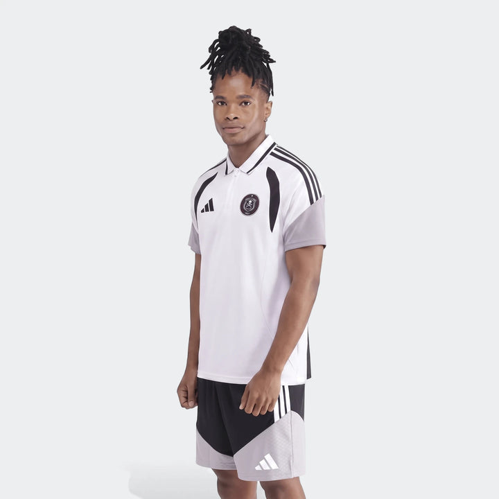 Male model wearing a white and black Adidas Op Tiro26C Polo shirt and matching black and grey shorts, full body view.