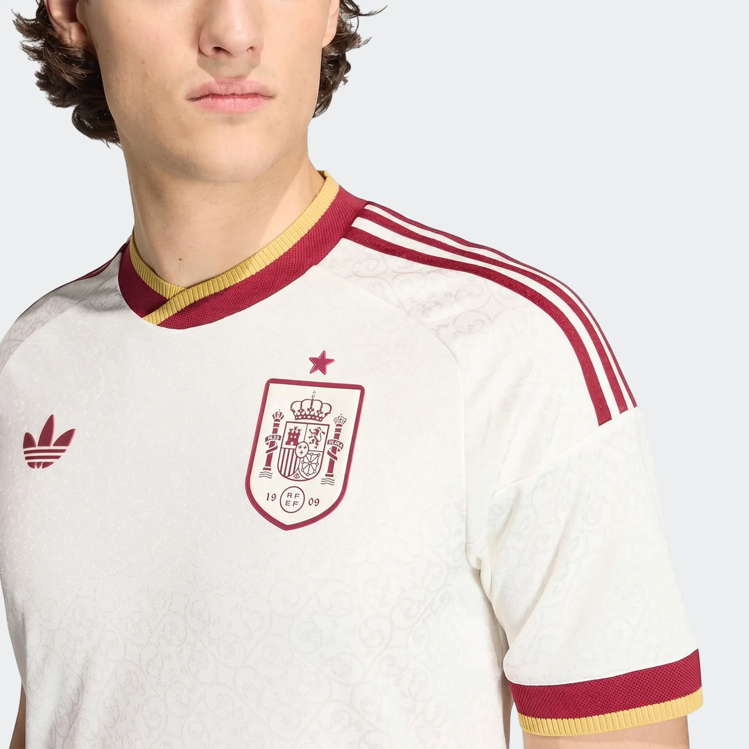 Close-up of a male model wearing a white Spain national football team away jersey with red and yellow details.