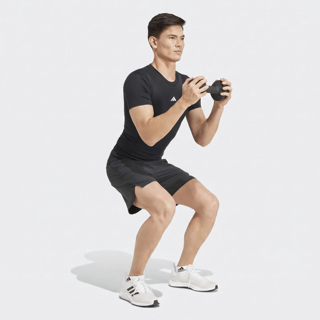 Man wearing a black Adidas short-sleeved Football T-Shirt and shorts, squatting while holding a dumbbell.