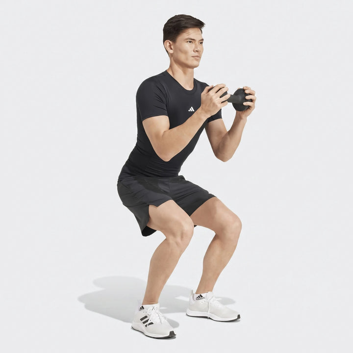 Man wearing a black Adidas short-sleeved Football T-Shirt and shorts, squatting while holding a dumbbell.