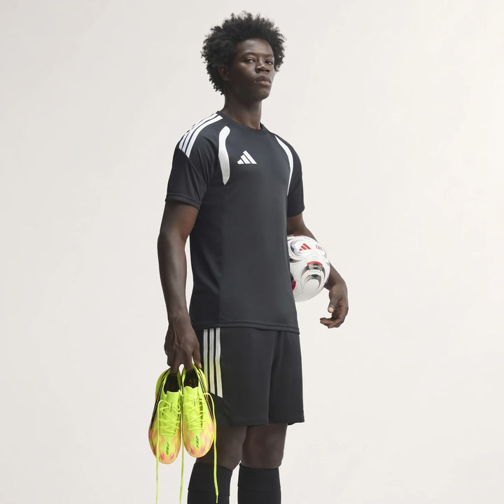 A man in a black football jersey and shorts holds a soccer ball and neon yellow F50 Hyperfast Elite Firm Ground Football