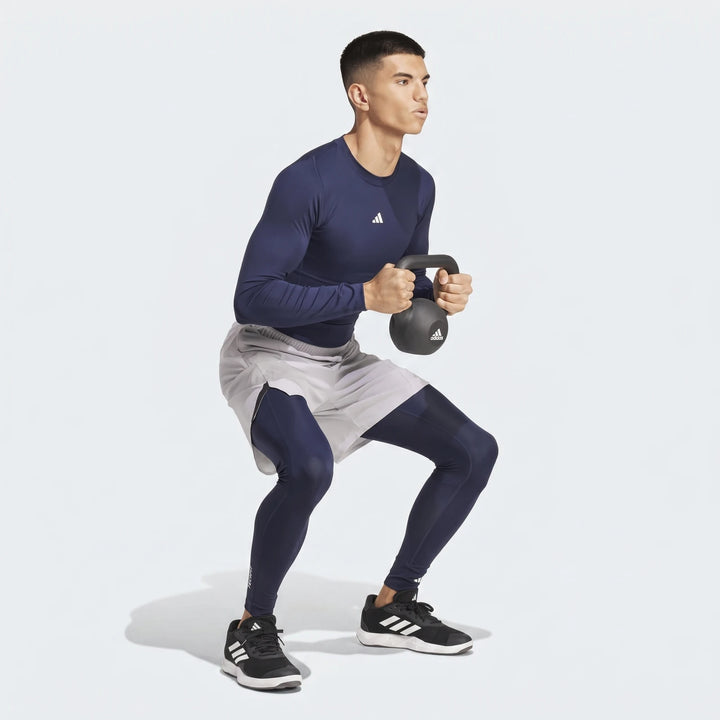 Man in navy blue Adidas Football Base Layer Tights, grey shorts, and a long-sleeve top performing a kettlebell squat.