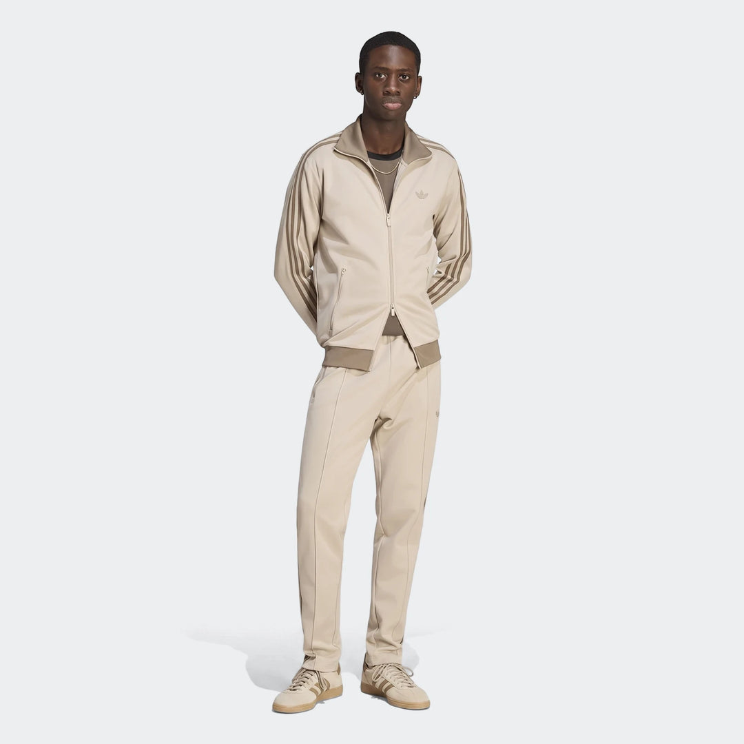 A man models beige Adidas Classic Track Pants and a matching track jacket, featuring the iconic three stripes, in a