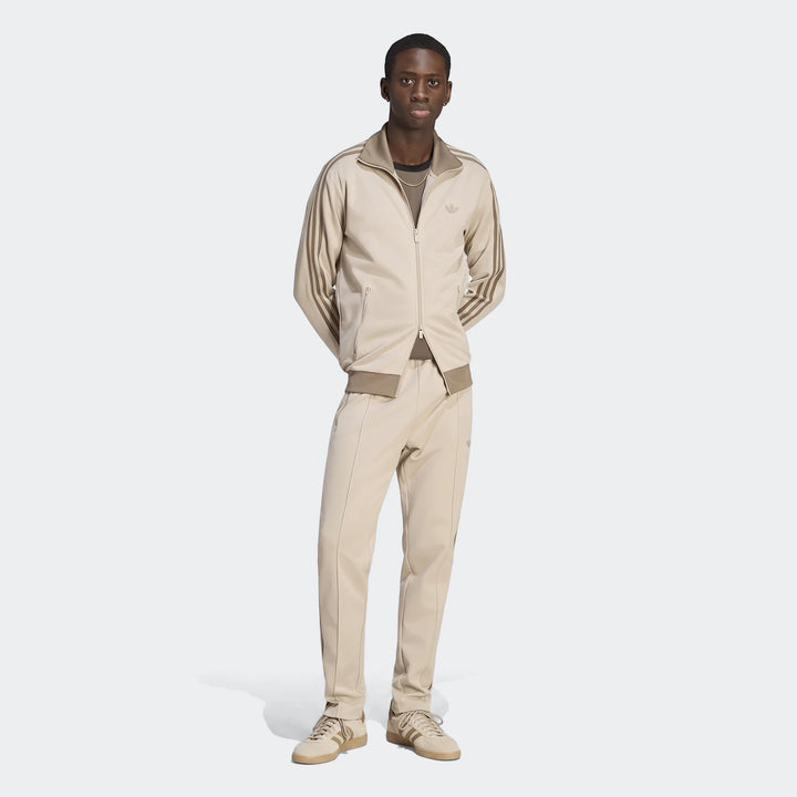 A man models beige Adidas Classic Track Pants and a matching track jacket, featuring the iconic three stripes, in a