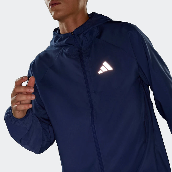 Man wearing a navy blue Adidas Run Essentials Jacket with a reflective logo and hood, shown from the front.