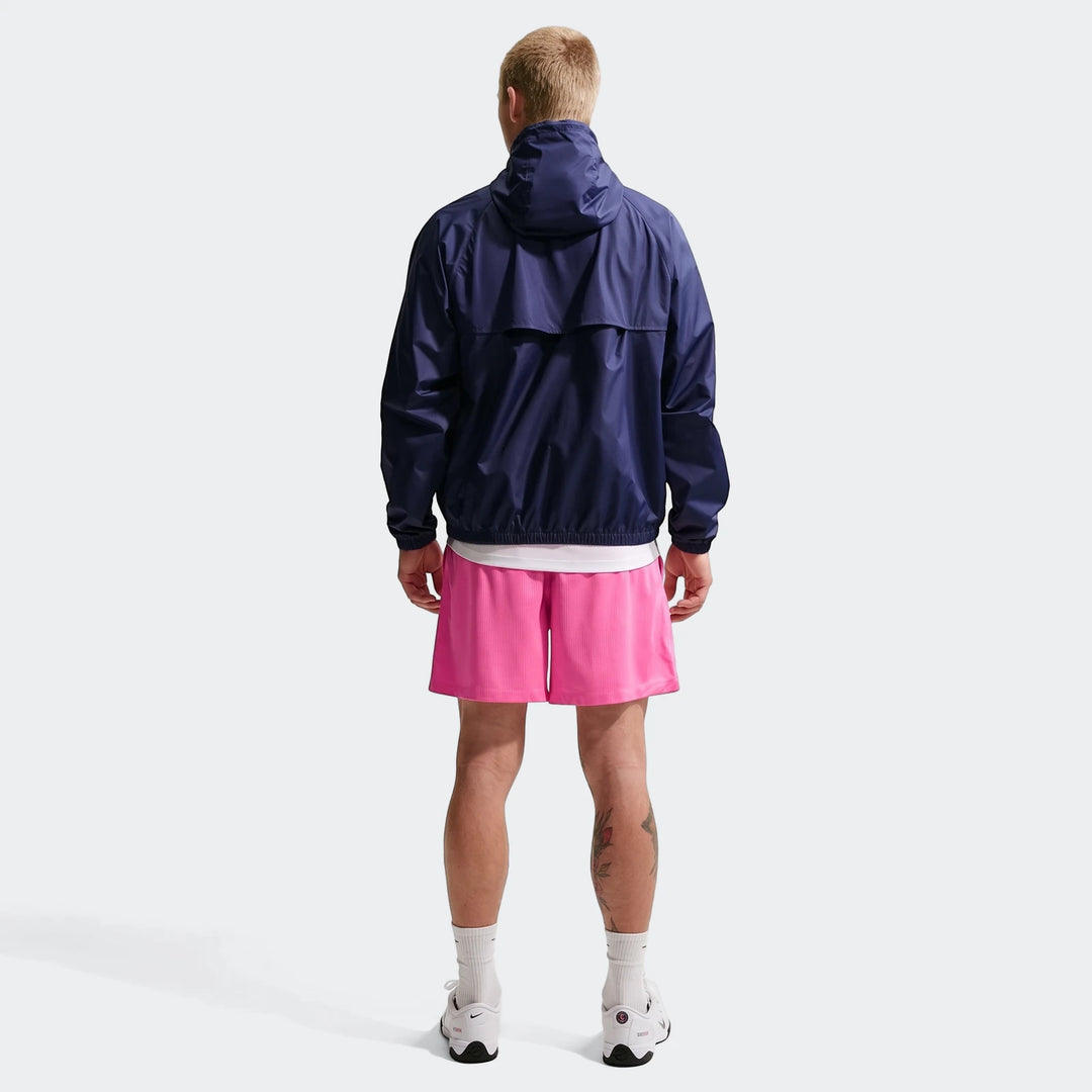 Rear view of a man wearing a navy blue hooded windbreaker jacket and pink Nike Sportswear Club Flow Shorts.