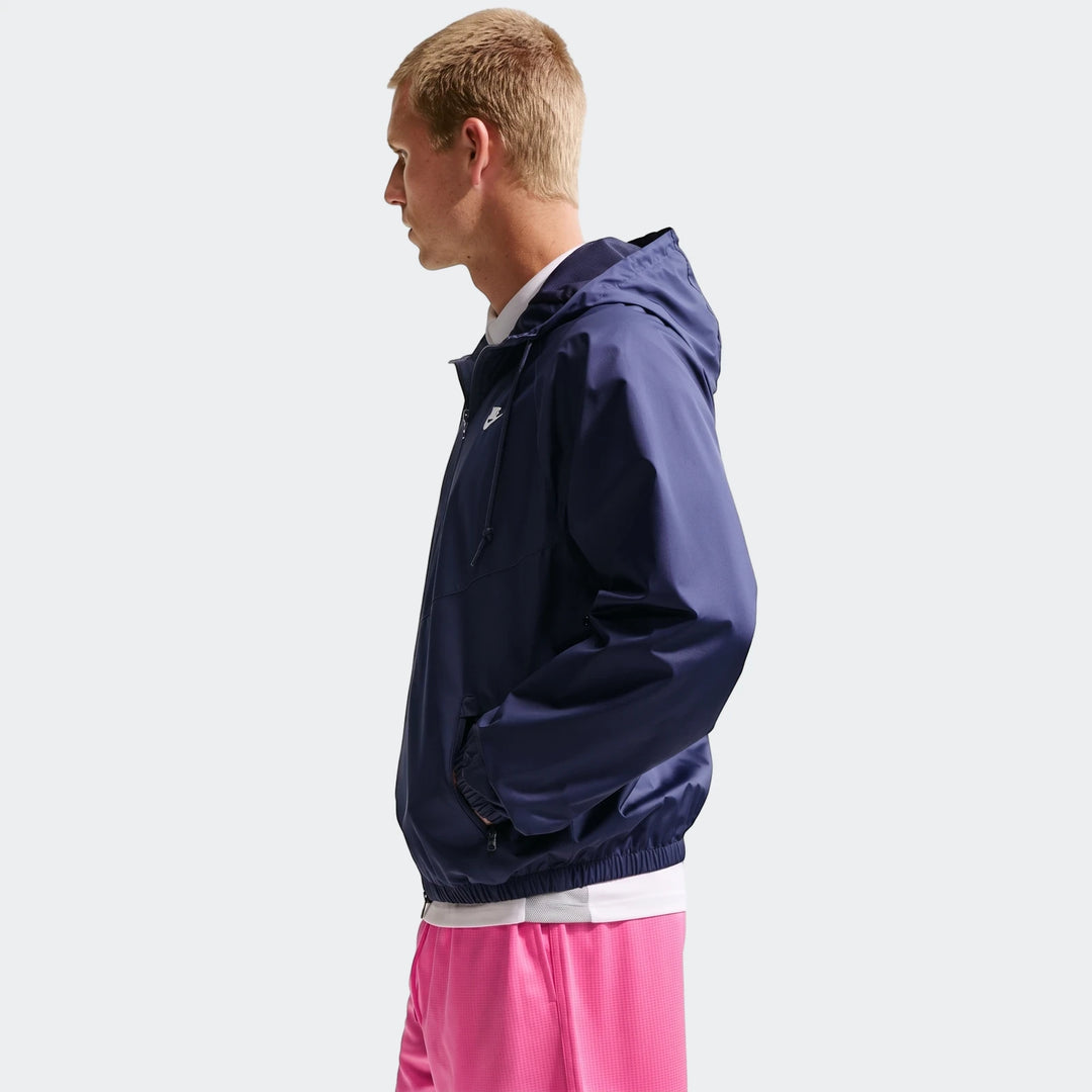 Profile view of a man wearing pink Nike Sportswear Club Red Men's Flow Shorts and a navy blue hooded jacket, hands in