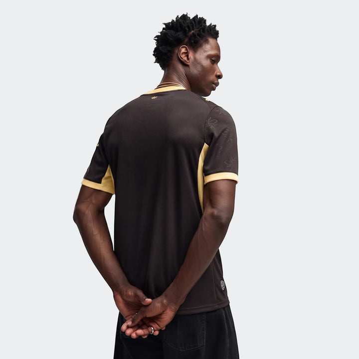 Back view of a man wearing the Manchester City 26/27 Away Jersey. The dark brown and gold men's football kit features subtle