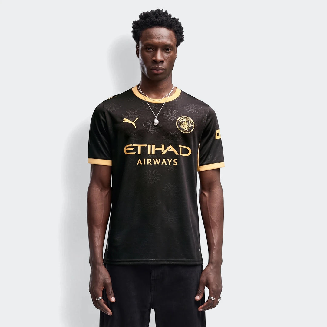 Manchester City 26/27 Away Jersey Men in black with gold accents, featuring bee pattern and team crest, worn by a male model.