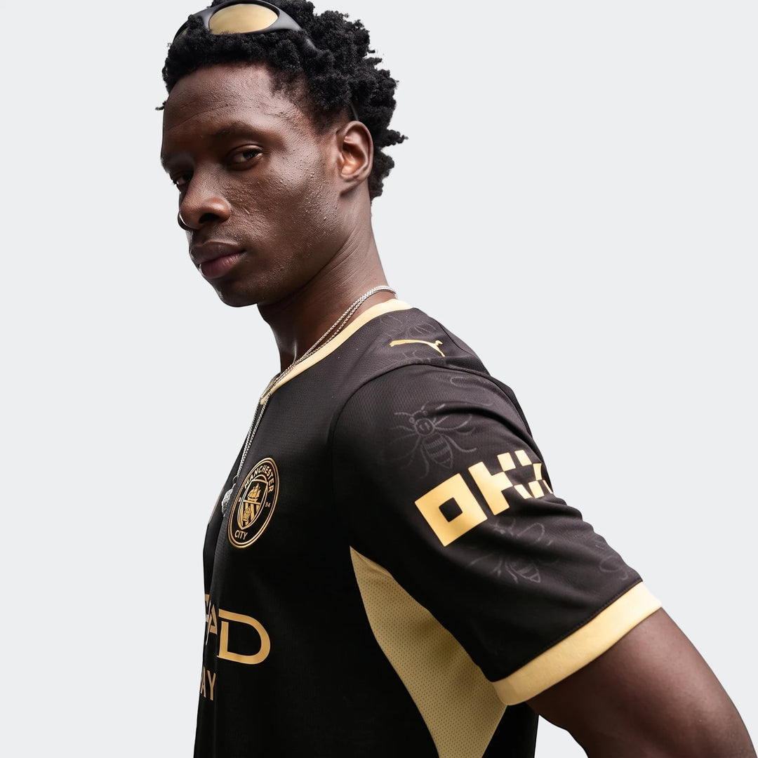 Close-up of a man wearing the black and gold Manchester City 26/27 Away Jersey, featuring the club crest and sponsor logos.