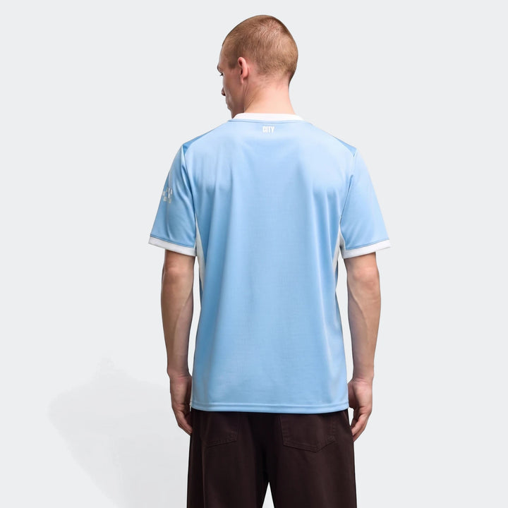 Back view of a man wearing the light blue Manchester City 26/27 Home Jersey for men, featuring white and gray accents.