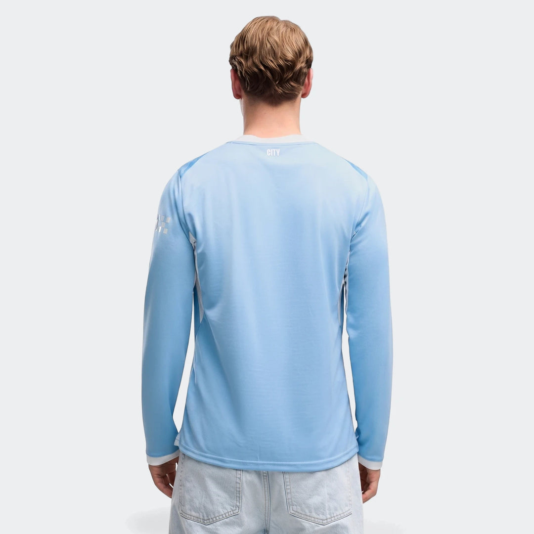 A man models the light blue Manchester City 26/27 Home Long Sleeve Jersey, shown from the back against a plain background,
