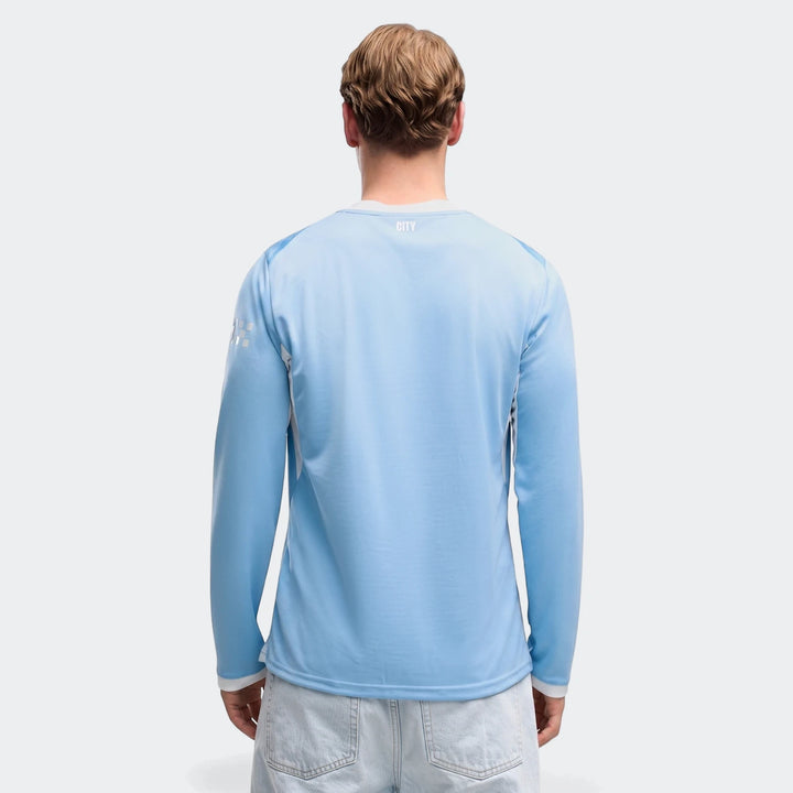 A man models the light blue Manchester City 26/27 Home Long Sleeve Jersey, shown from the back against a plain background,