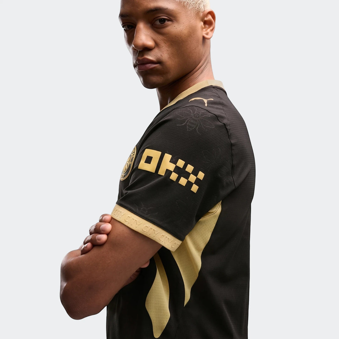 Male model in black and gold Manchester City Away Authentic Jersey with arms crossed, showing team crest and OKX logo.