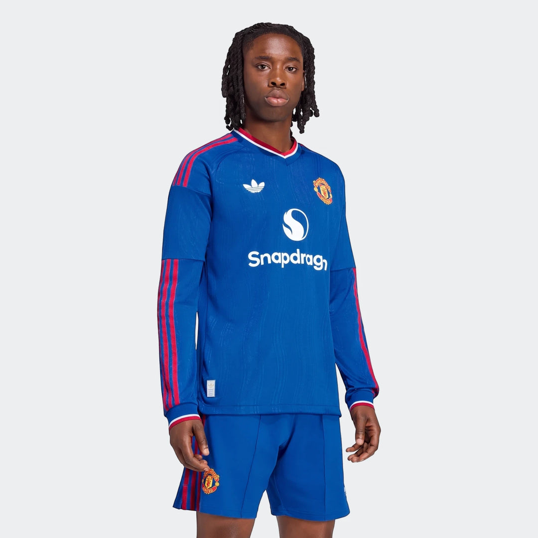 Male model wearing a blue Manchester United 26/27 Away Authentic Longsleeve Jersey with red stripes and matching shorts.