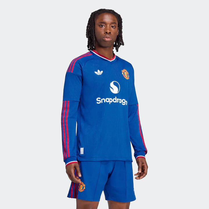 Male model wearing a blue Manchester United 26/27 Away Authentic Longsleeve Jersey with red stripes and matching shorts.