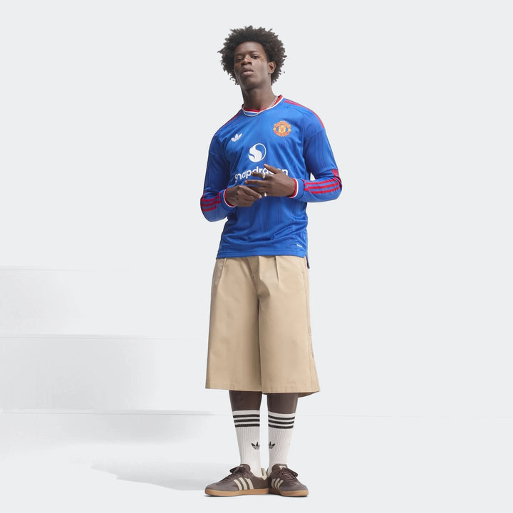 A male model wearing a blue Manchester United 26/27 Away Authentic Longsleeve Jersey, paired with khaki shorts and sneakers.