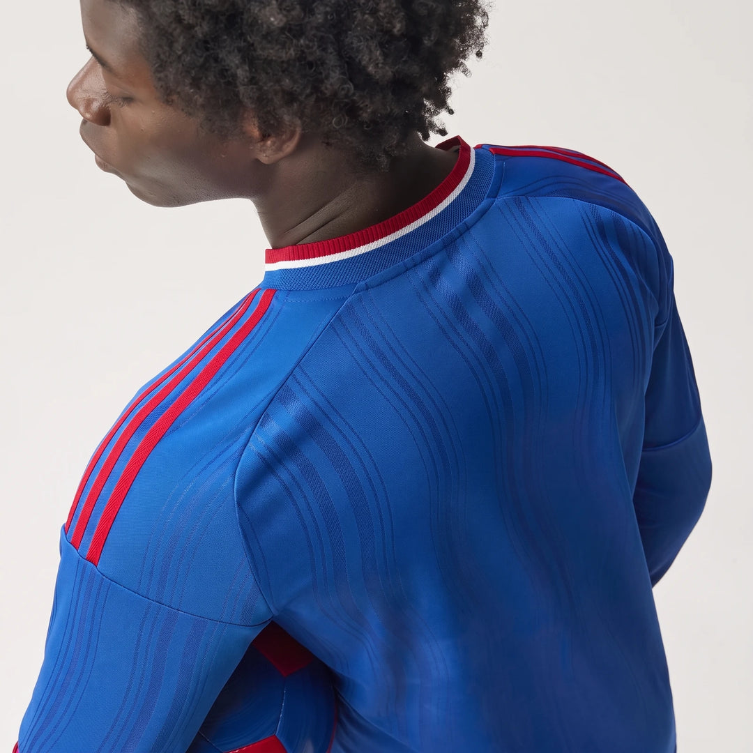 A dark-skinned person wearing a blue Manchester United 26/27 Away Authentic Longsleeve Jersey with red stripes, shown from