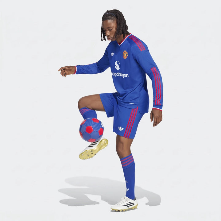 A male model wearing a blue Manchester United 26/27 Away Authentic Longsleeve Jersey and matching shorts, juggling a soccer