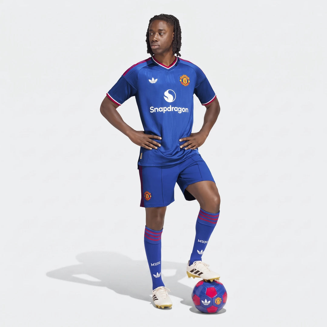 Male model wearing a blue Manchester United 26/27 Away Authentic Jersey, matching shorts, and socks, standing with a soccer