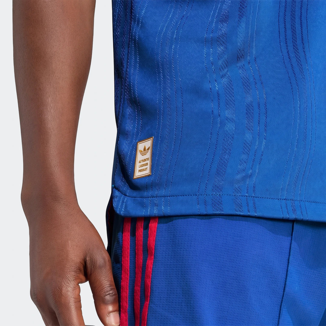 Close-up of a person wearing an authentic blue Manchester United 26/27 away jersey, featuring a golden Adidas product tag