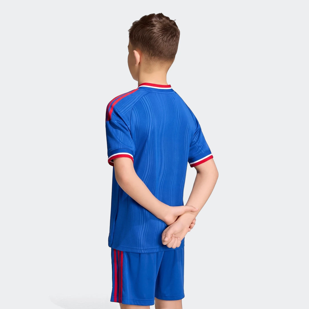 Back view of a young boy wearing a blue Manchester United 26/27 Away Kids Jersey with red stripes and matching shorts.