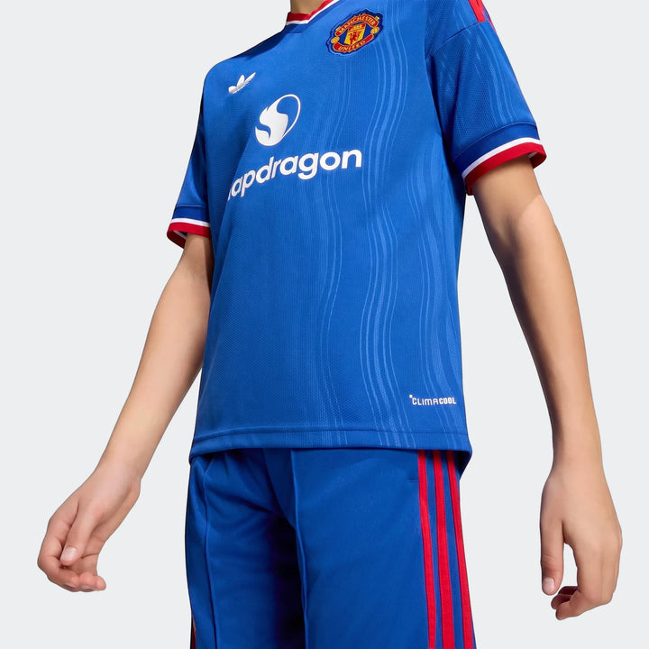 Kid wearing blue Manchester United 26/27 away jersey and matching shorts with red stripes and club crest.