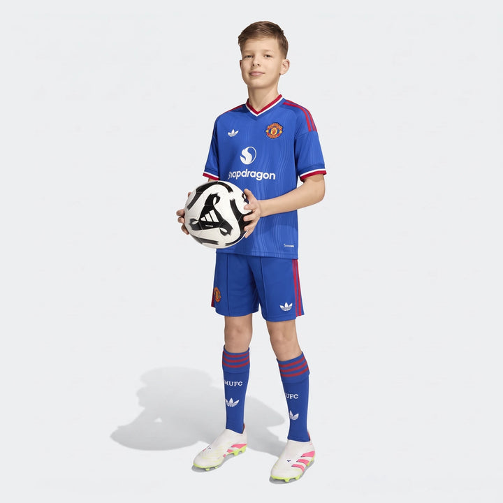 Boy wearing a blue Manchester United 26/27 Away Jersey, shorts, and socks, holding a soccer ball.