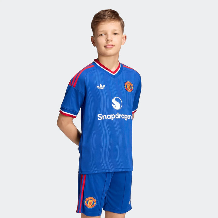 Young boy wearing a full Manchester United 26/27 Away Jersey Kids kit with blue jersey and matching shorts, front view.