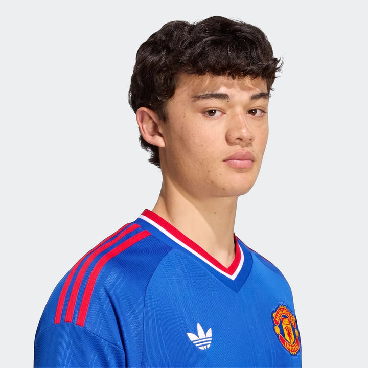 Young man wearing a blue Manchester United 26/27 Away Longsleeve Jersey with red stripes and club crest.